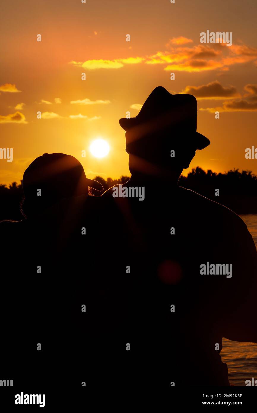 Silhouette eines Mannes, der seinen Sohn umarmt und den Sonnenuntergang in Key West, Florida, USA, beobachtet Stockfoto