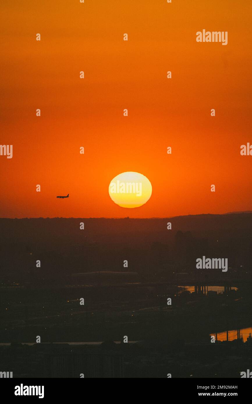 Malerischer Blick auf den farbenfrohen, orangefarbenen Sonnenuntergang mit der runden, großen gelben Sonne und dem fliegenden Flugzeug Stockfoto