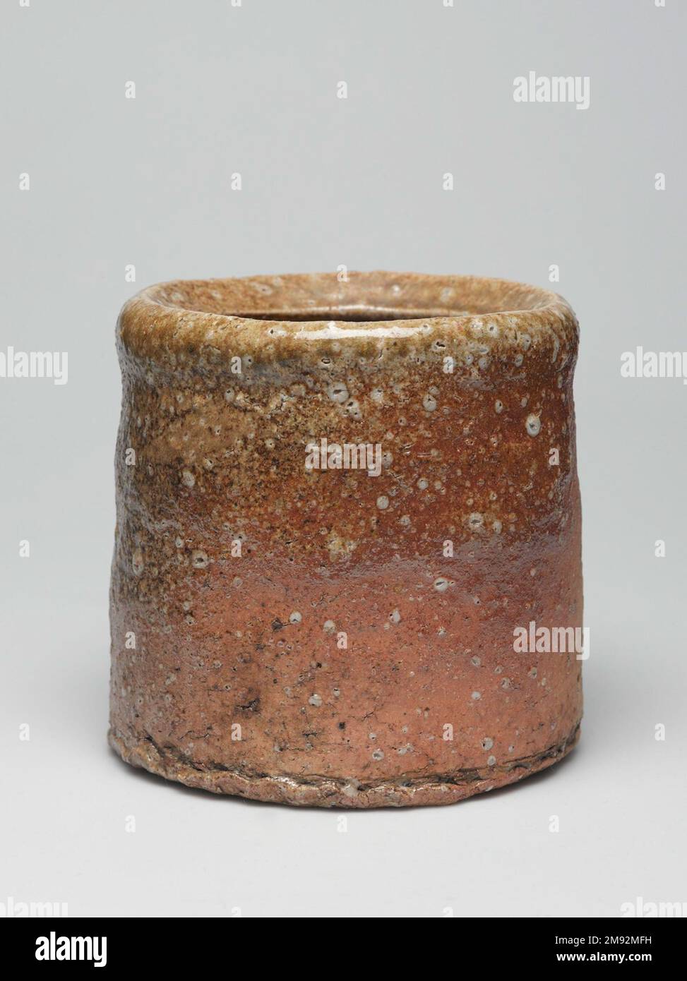 Shigaraki Ware Mizusashi (Teezeremonie Süßwasserdose) Shigaraki Ware Mizusashi (Teezeremonie Süßwasserdose), ca. 1620" Steingut mit Ascheglasur, Lackdeckel; Shigaraki-Geschirr, 6 x 6 1/2" (15,2 x 16,5 cm). Während die meisten Töpfer darauf achten, Steine aus ihrem Lehm zu filtern, verstehen die Töpfer aus der Region Shigaraki, dass die durch steinige Quarzstücke und Feldspat erzeugte Textur ihre Waren taktil und visuell interessant macht. Die Handwerker fügen nur minimale Glasur hinzu, sodass die Oberfläche ihre Körnung behält. Shigaraki, östlich von Kyōto, ist seit Jahrhunderten eine Ofenanlage, die ursprünglich hergestellt wurde Stockfoto