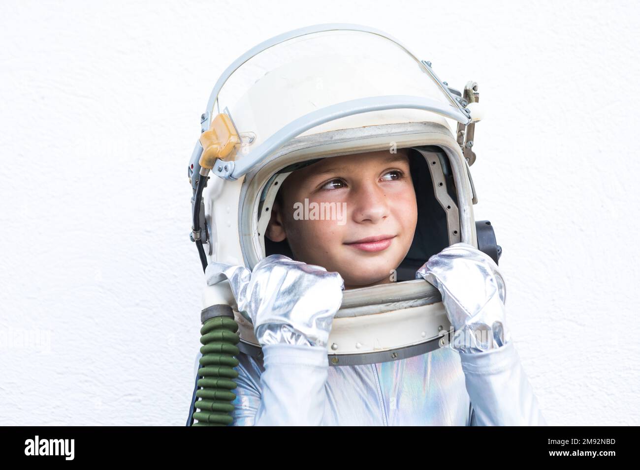 Isoliertes Kind im silbernen Weltraumanzug, das den Helm berührt und vor weißem Hintergrund aufblickt Stockfoto