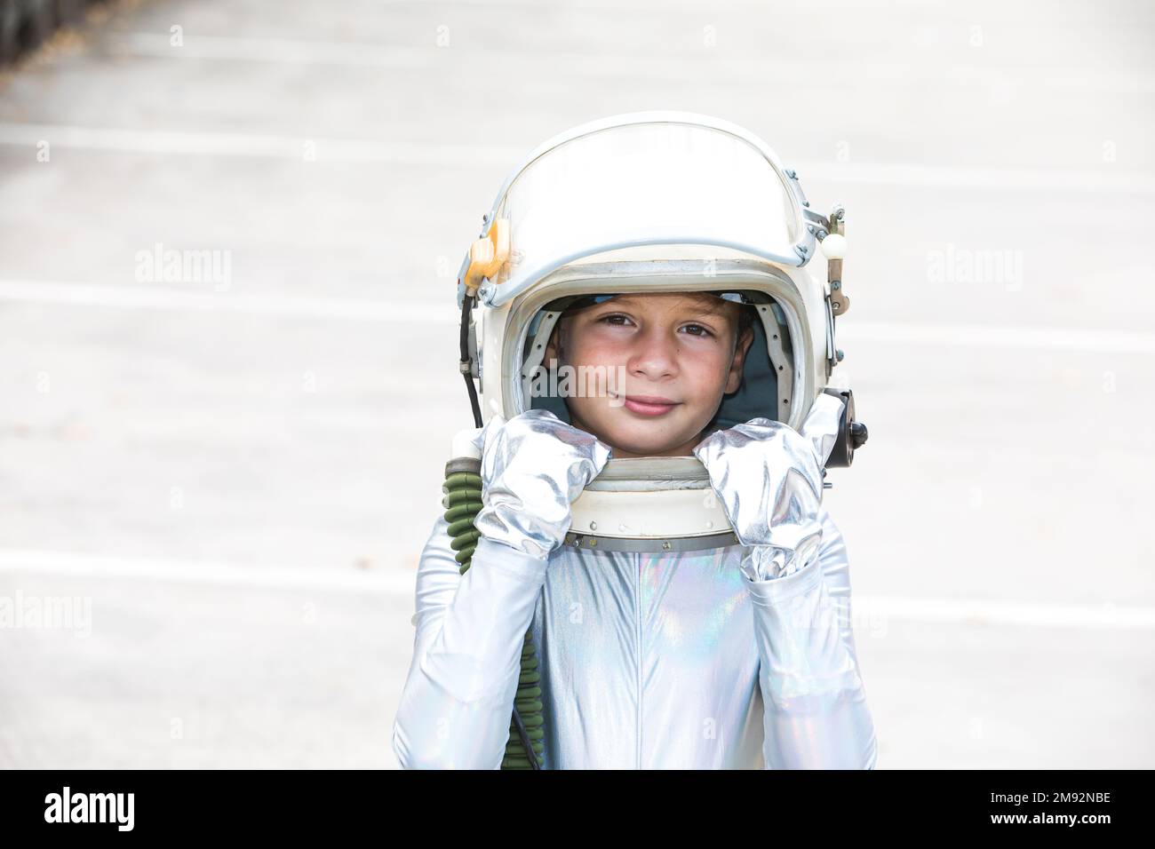 Glückliches, isoliertes Kind im silbernen Raumanzug, das den Helm berührt und in die Kamera schaut, während es vor weißem Hintergrund steht Stockfoto