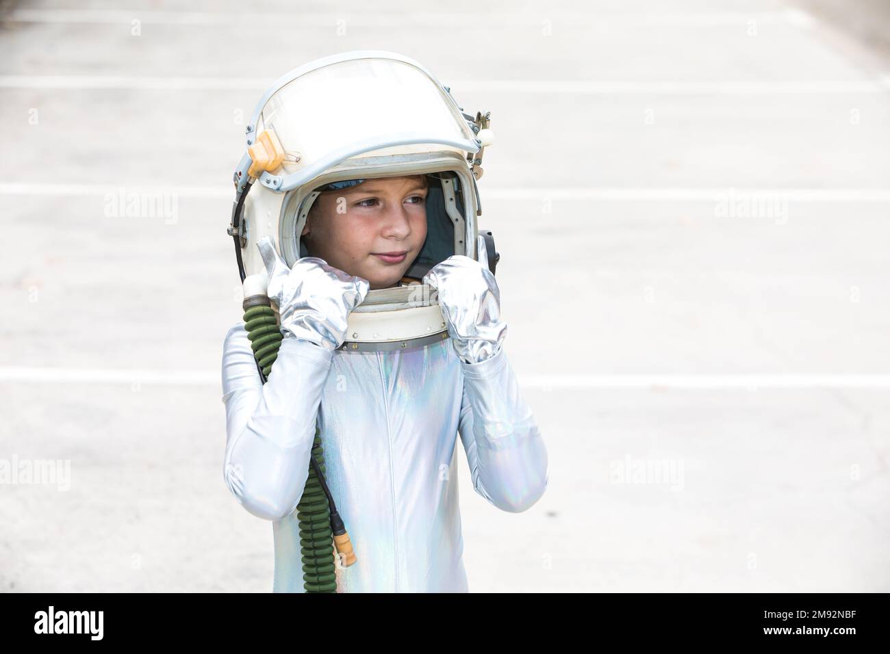 Isoliertes Kind im silbernen Raumanzug, das den Helm berührt und wegschaut, während es vor weißem Hintergrund steht Stockfoto