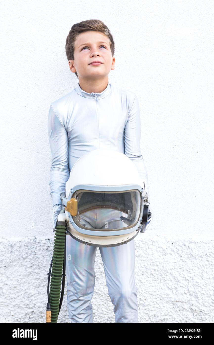 Isoliertes Kind im silbernen Weltraumanzug, das den Helm berührt und vor weißem Hintergrund aufblickt Stockfoto