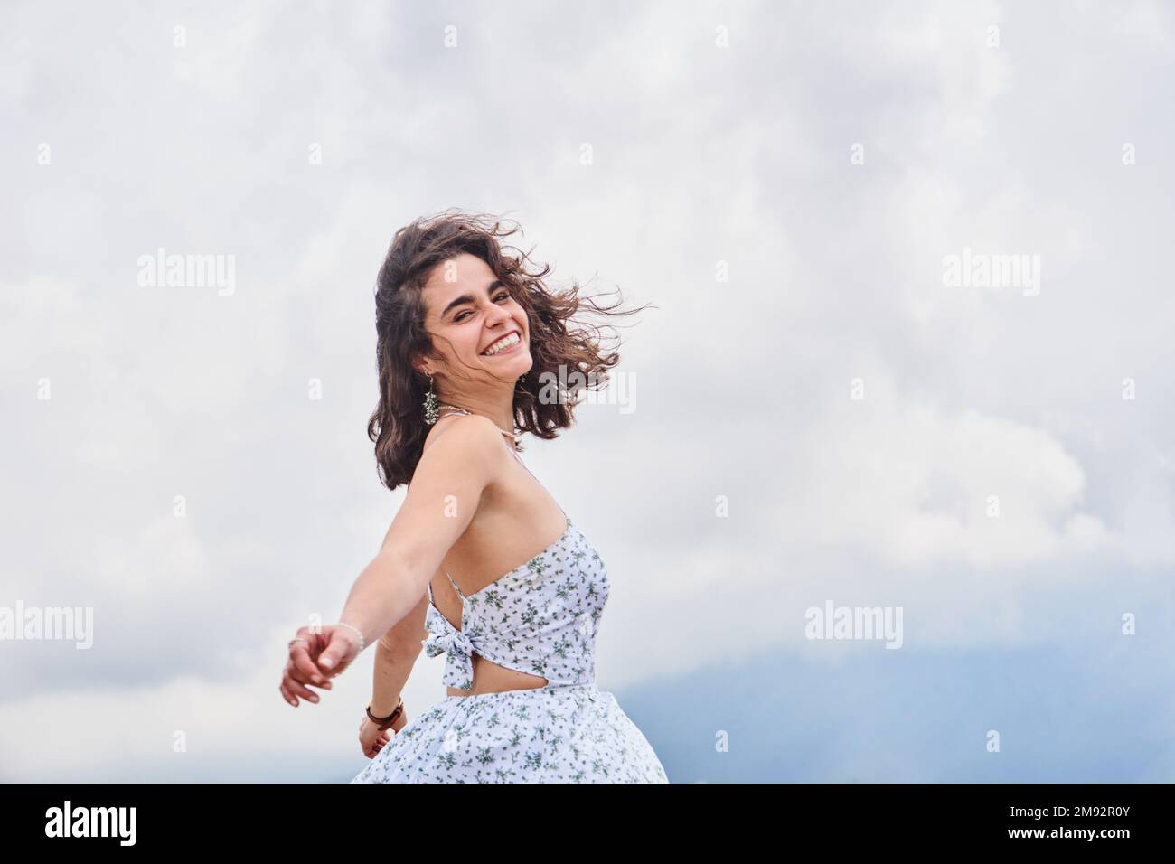 Kleiner Winkel einer glücklichen jungen Frau in weißem Sommerkleid, die lächelt und den Tag genießt, während sie vor der Kamera tanzt Stockfoto