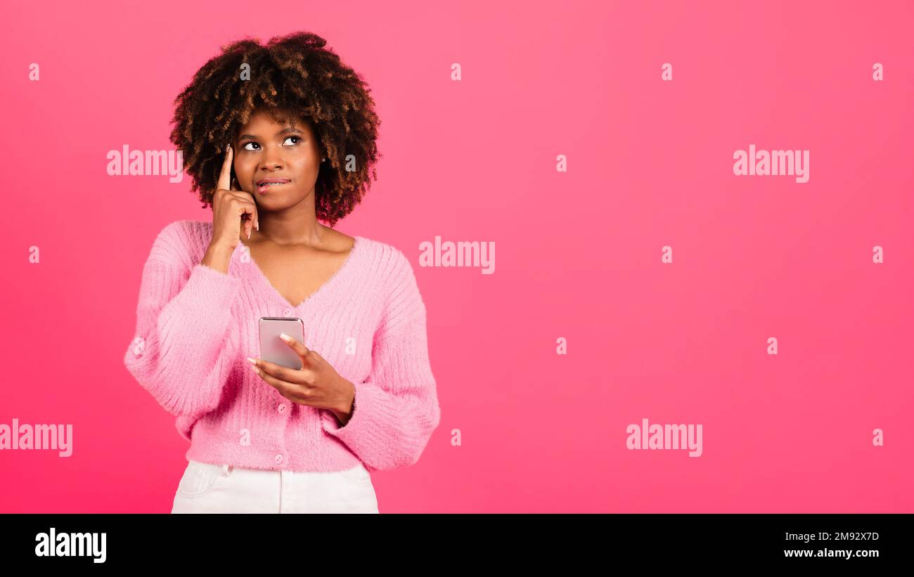 Nachdenkliche, afroamerikanische Millenialleiterin mit geschweiften Klammern in lässigem Denken, benutzt Telefon, sieht sich Kopierraum an Stockfoto