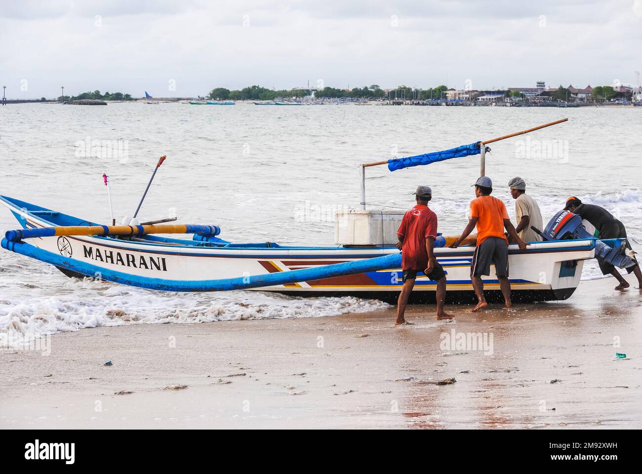 Bali, Indonesien - ca. Februar 2017: Fischer, die ihre Jukung ins Meer bekommen. Ein Jukung ist ein traditionelles balinesisches Fischerboot. Stockfoto