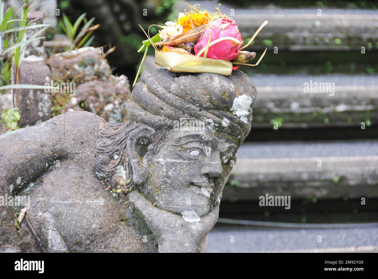 Balinesisches religiöses Angebot (Canang sari) über einer Steinstatue. Stockfoto