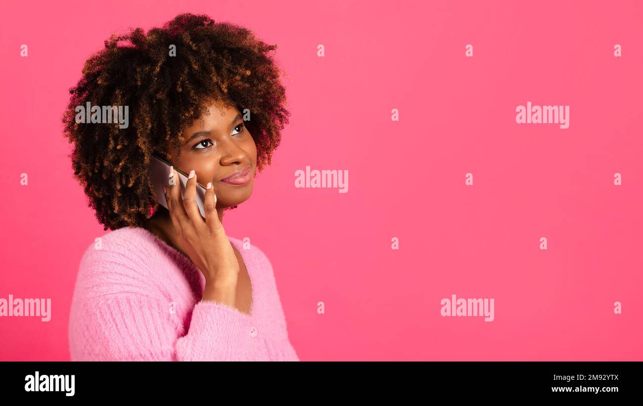 Glückliche, nachdenkliche, afroamerikanische, lockige Frau, die gelegentlich telefoniert, schau dir den Kopierraum an Stockfoto