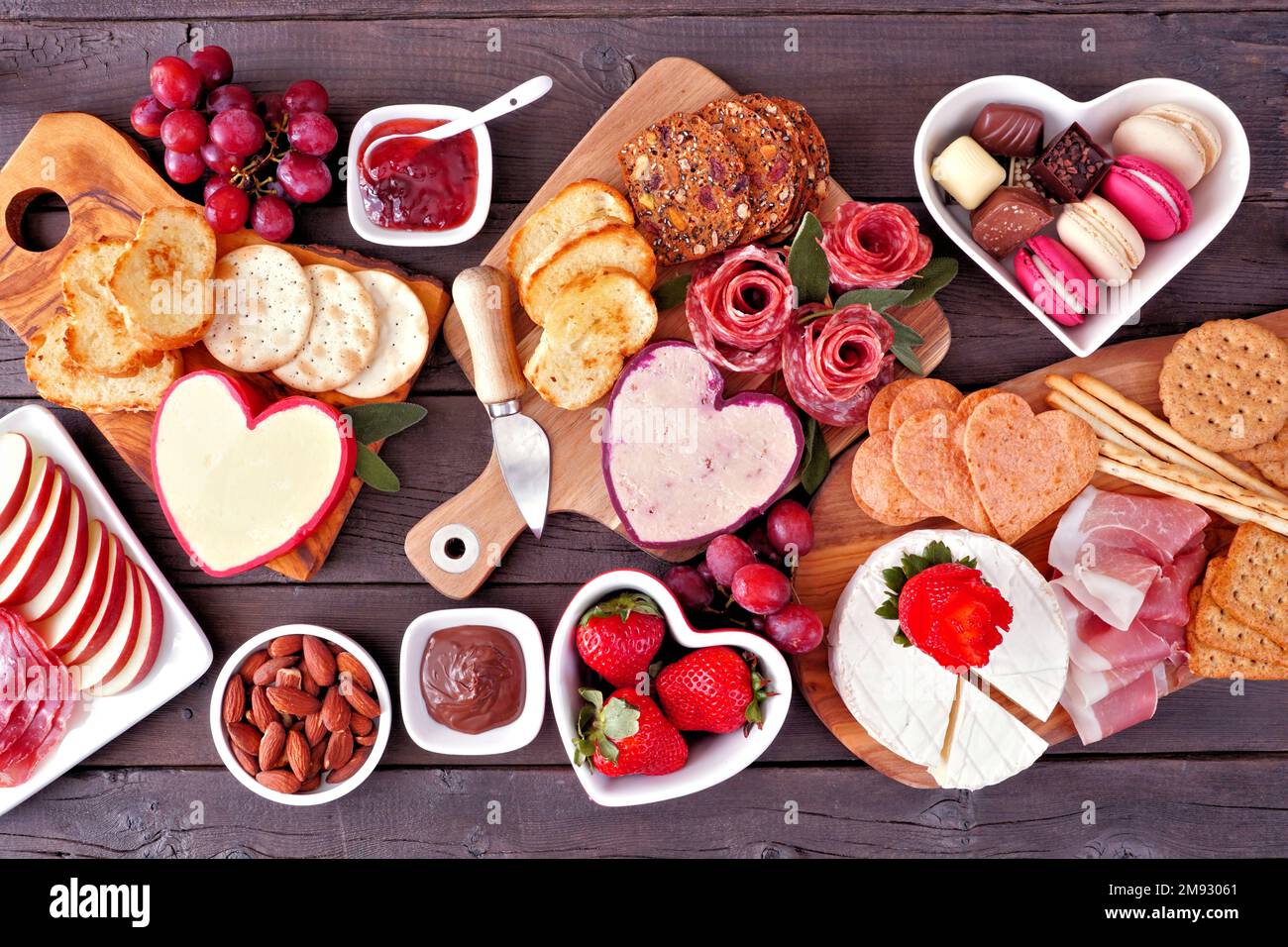 Tischszene zum Valentinstag mit Wurstwaren vor dunklem Holzhintergrund. Verschiedene Käse-, Fleisch-, Obst- und süße Vorspeisen. Ansicht von oben nach unten. Stockfoto