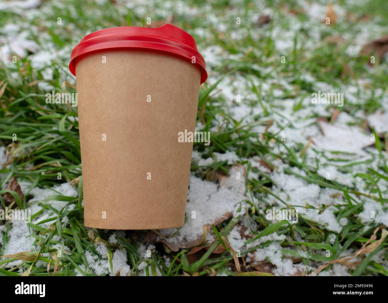 Im Winter. Kaltes Wetter. Der Boden ist mit einer kleinen Schneeschicht bedeckt. Eine Tasse Kaffee liegt auf dem Rasen (Nahaufnahme) Stockfoto