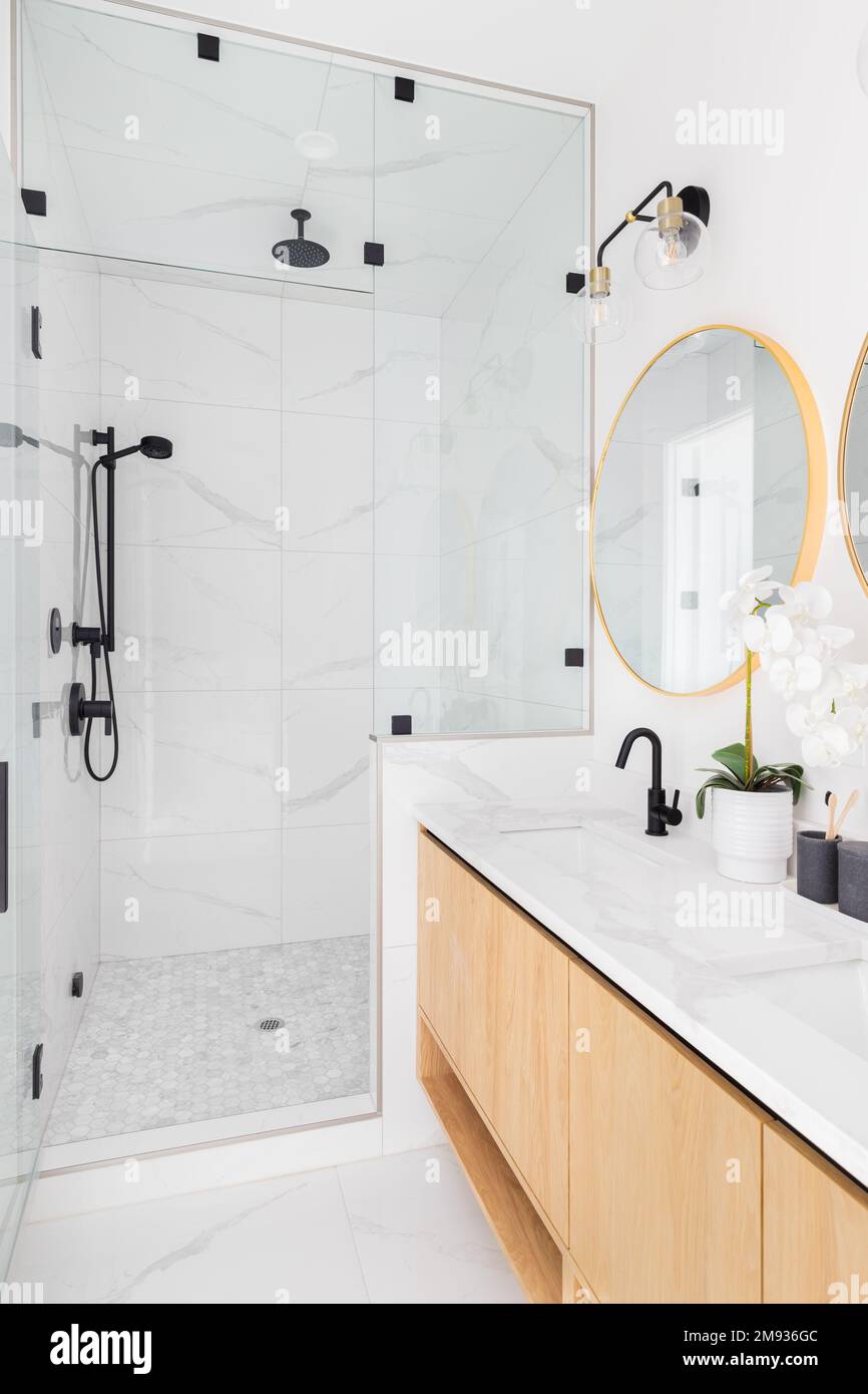 Luxuriöses Badezimmer mit schwimmendem Holzschrank, Marmorablagefläche, goldenen Spiegeln und marmorgefliester Duschkabine. Stockfoto
