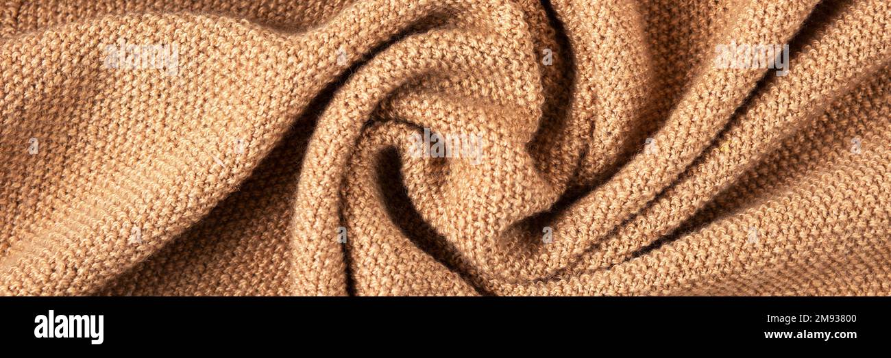 Gestrickter beigefarbener Hintergrund. Nahaufnahme einer Strickdecke. Wellenförmig faltet Material. Strickpullover oder -Mantel in warmem Beige. Banner Stockfoto