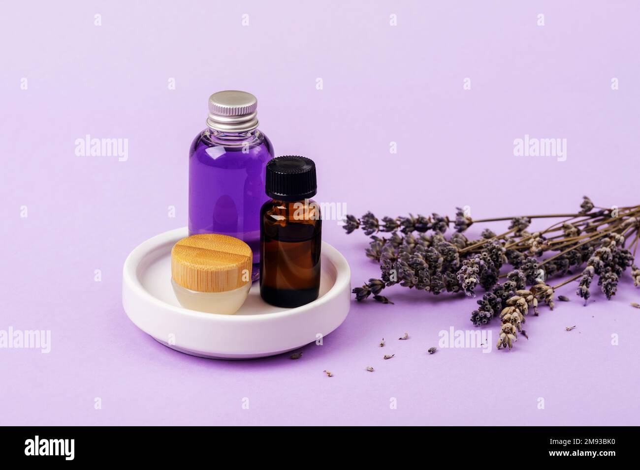 Ätherisches Lavendelöl, Serum und Sahne auf weißem Gericht und getrockneten Lavendelblumen. Hautpflege, Aromatherapie, Selbstpflegekonzept. Nahaufnahme. Stockfoto