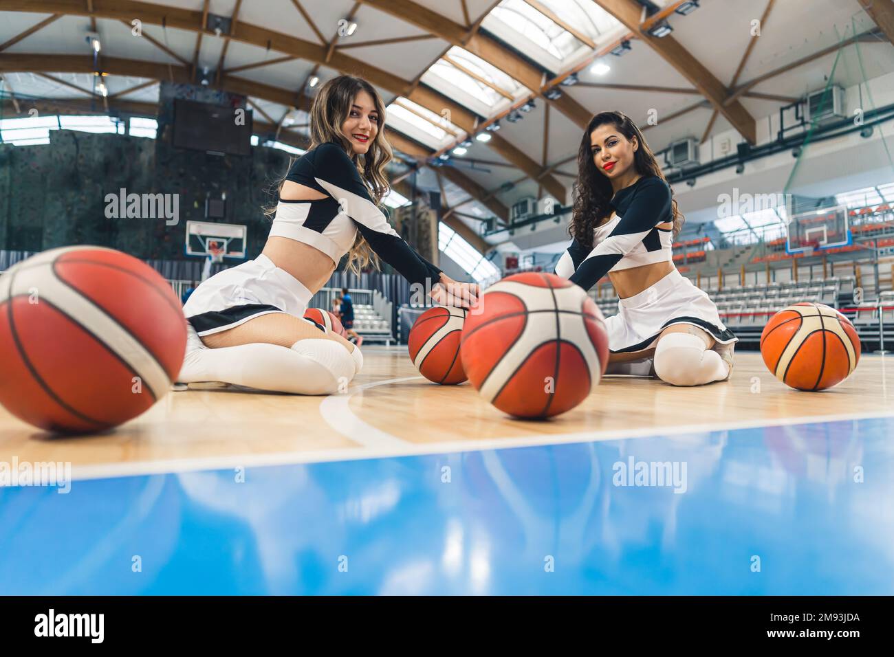 Ein kleiner Schuss von zwei Cheerleader, die mit Basketbällen auf dem Boden des Fitnessstudios sitzen. Sportkonzept. Hochwertiges Foto Stockfoto