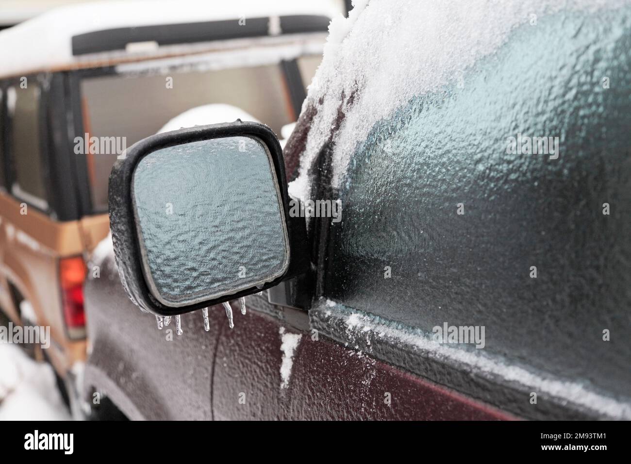 Geparkte SUV mit Eis und Schnee an einem Wintertag. Konzentriere dich auf den vereisten Seitenspiegel Stockfoto