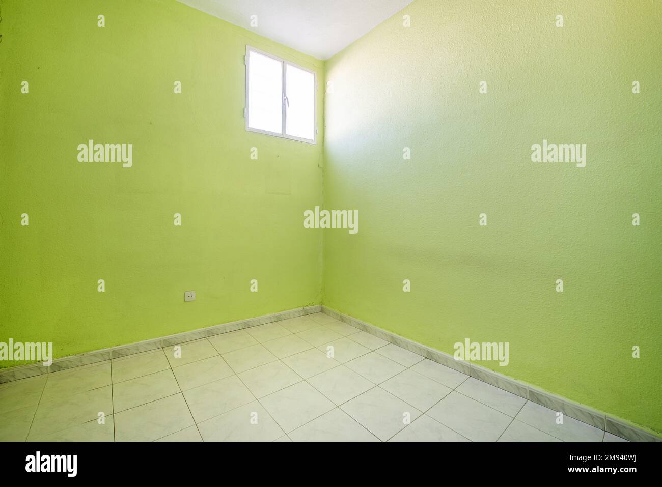 Leerer Raum mit pistaziengrün bemalten Wänden mit weißem Fliesenboden und einem einzigen Aluminiumfenster in einer Ecke Stockfoto