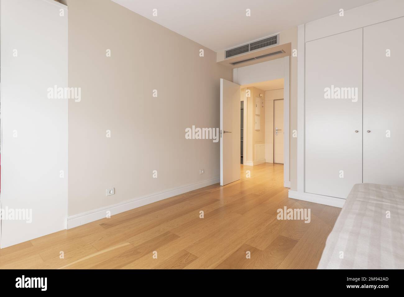 Schlafzimmer mit einem Einzelbett mit einer hellen Bettdecke und einem eingebauten Kleiderschrank mit weißen Türen und Klimaanlage durch Kanäle in der abgehängten Decke Stockfoto