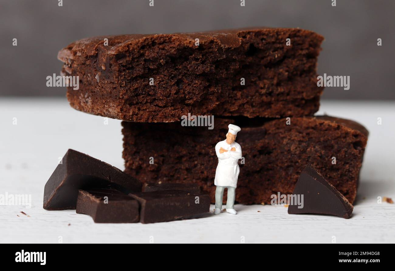 Schokoladenbrownie im Ofen gebacken und ein Minikoch. Miniaturmenschen und Schokoladenbrownie mit Geschäftskonzept. Stockfoto
