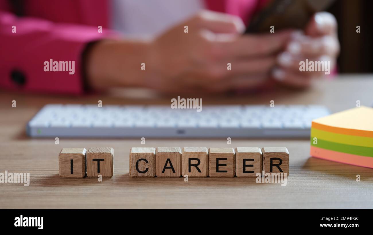 IT-Spezialist, der am Büroschreibtisch an der Tastatur arbeitet, Holzwürfel mit Worten IT-Karriere vor sich. Stockfoto