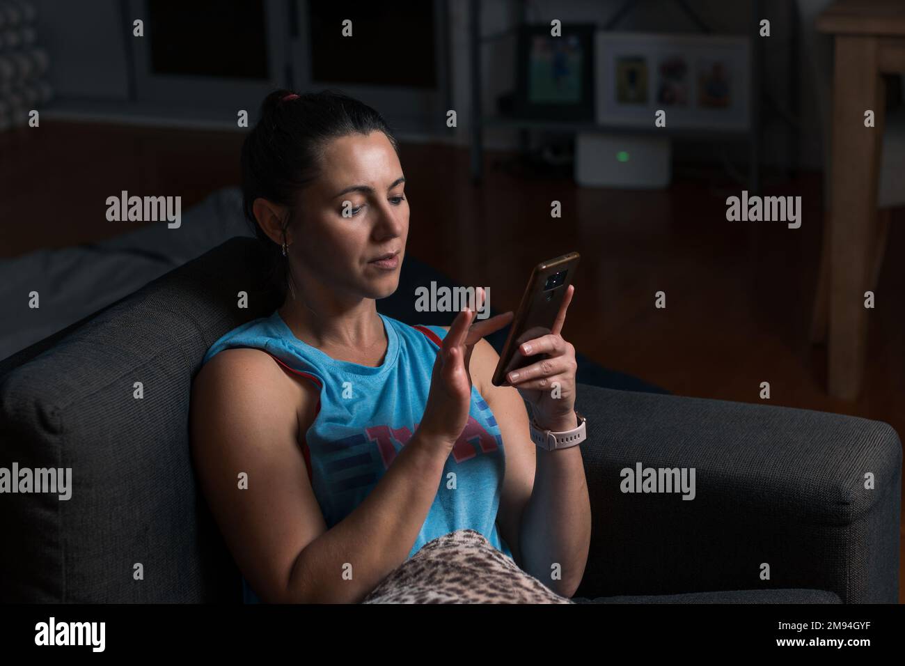 Eine wunderschöne junge Frau, die auf dem Sofa im Wohnzimmer sitzt und mit ihrem Smartphone surft Stockfoto