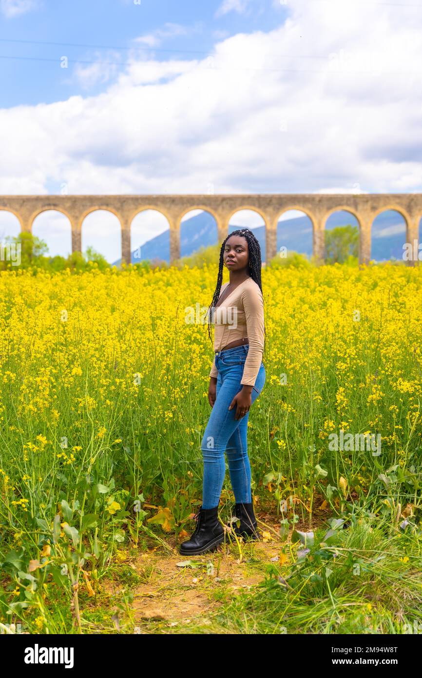 Lachte lächelnd, schwarzes ethnisches Mädchen mit Zöpfen, Reisende, auf einem Feld gelber Blumen Stockfoto