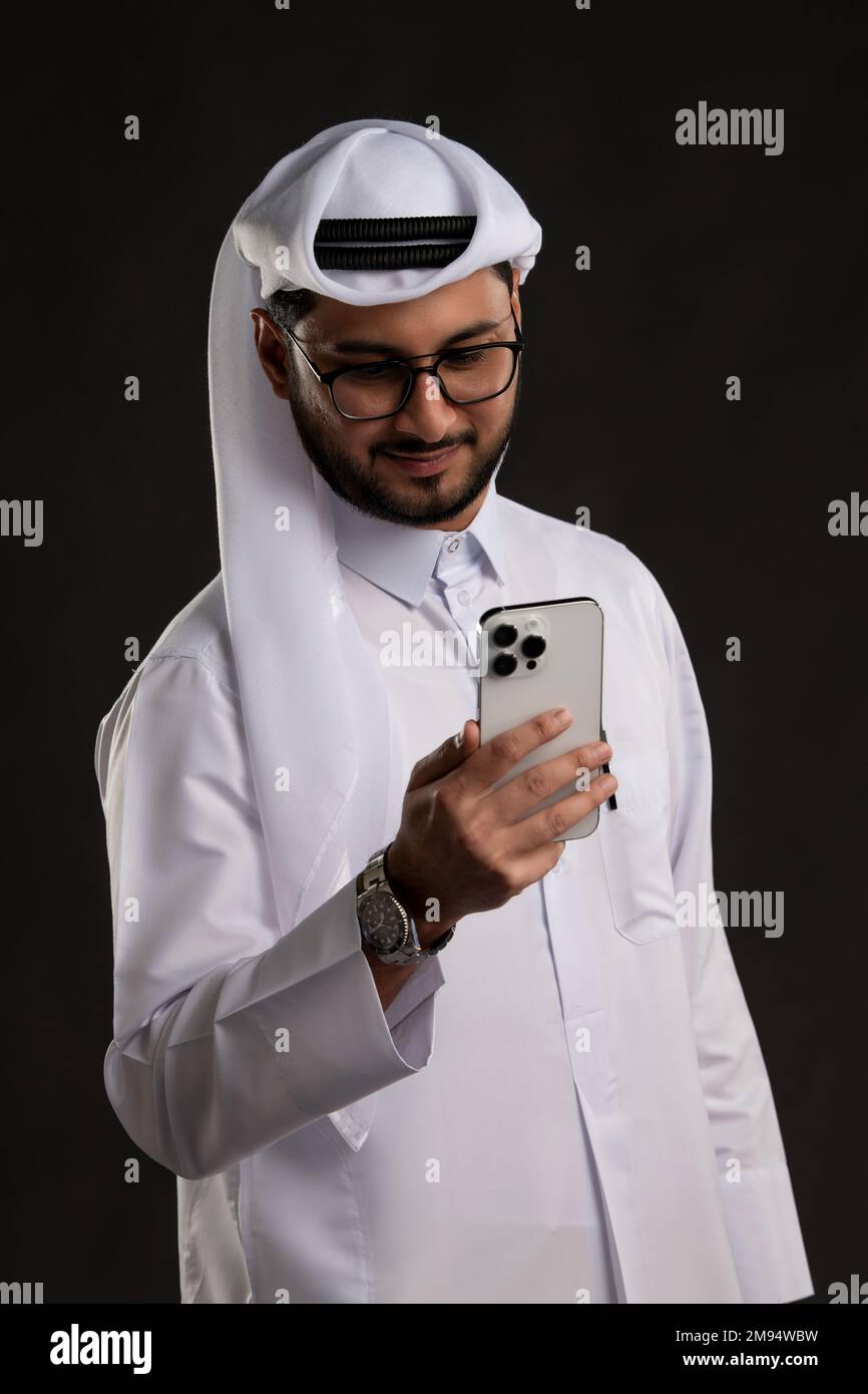 Arabischer Katar-Mann, der Tisch benutzt und auf isoliertem Hintergrund posiert. Männliches Modell in arabisch-katarischem Kleid auf isoliertem Hintergrund. Verschiedene Posen Stockfoto