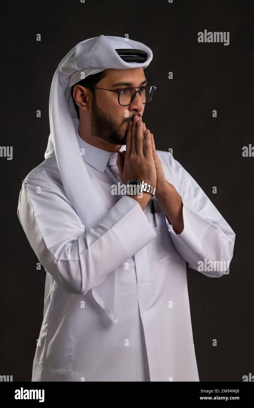 Arabischer Katar-Mann, der Tisch benutzt und auf isoliertem Hintergrund posiert. Männliches Modell in arabisch-katarischem Kleid auf isoliertem Hintergrund. Verschiedene Posen Stockfoto