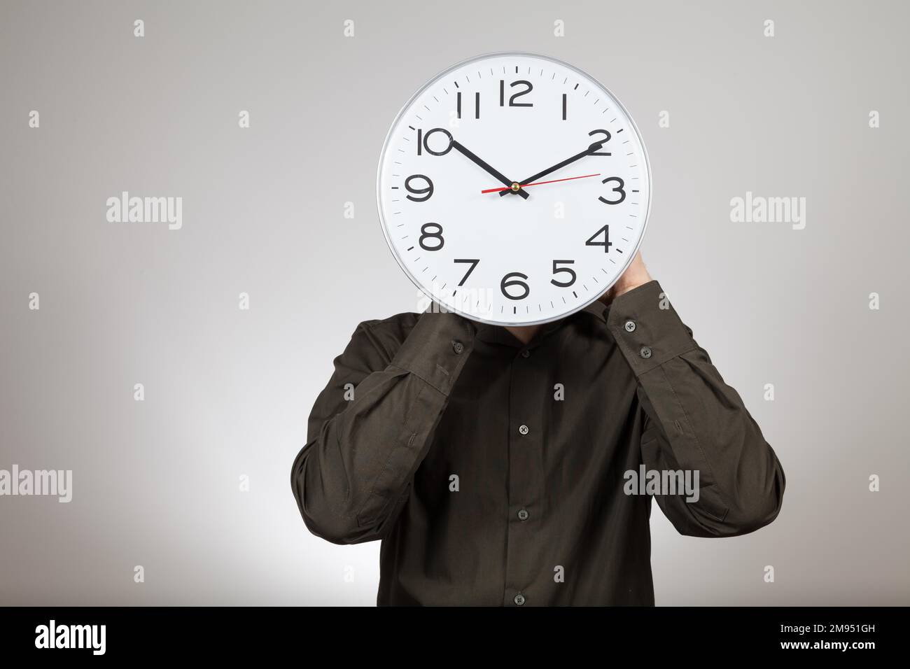 Symbolisches Bild der Arbeitszeit, Mann hält eine Uhr vor seinem Gesicht Stockfoto