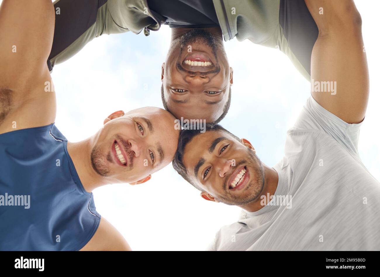 Nur drei Kumpels bauen Muskeln zusammen. Aufnahme einer Gruppe sportlicher junger Menschen aus dem unteren Winkel, die sich im Freien zusammentun. Stockfoto