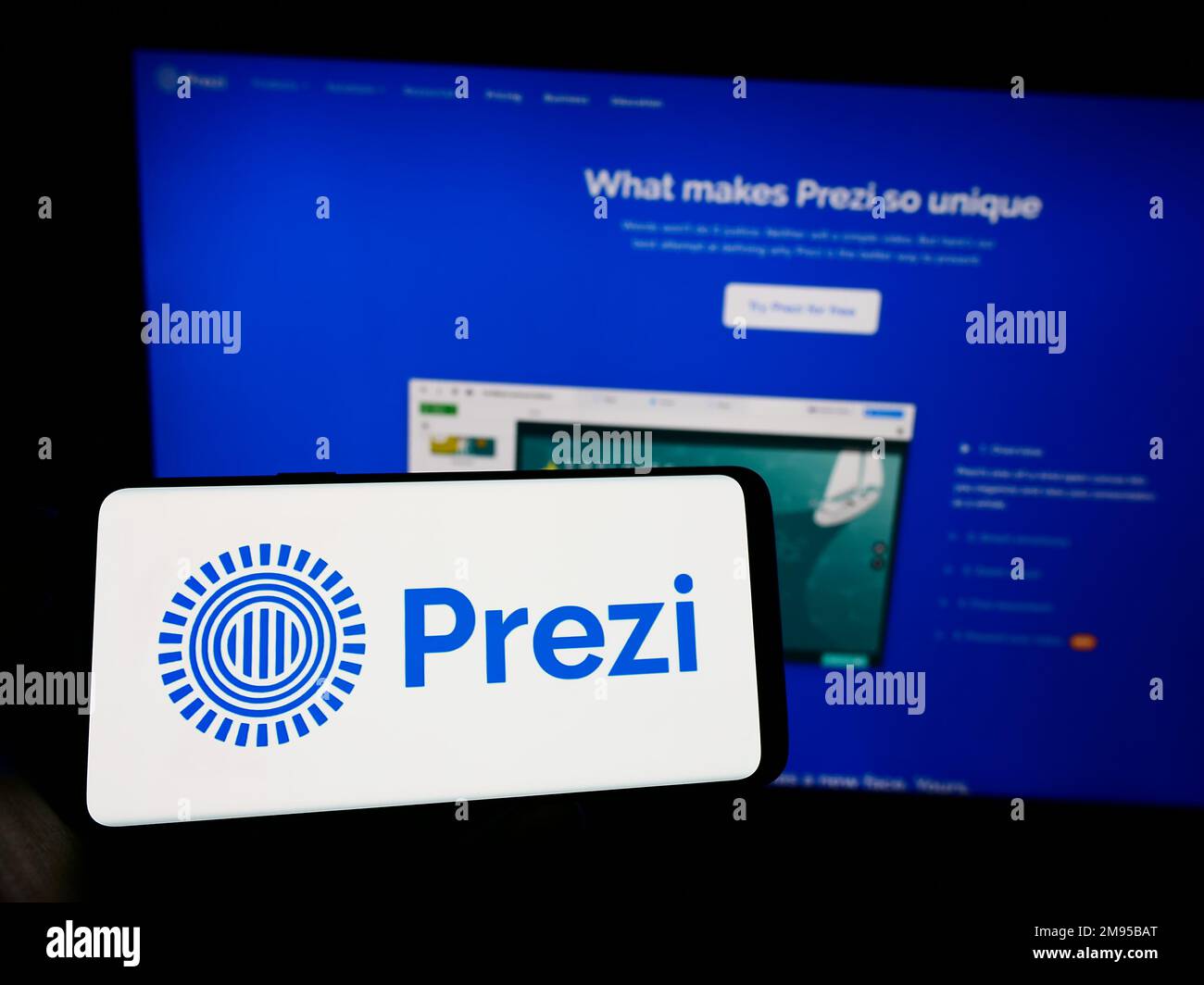 Person, die ein Mobiltelefon mit dem Logo des ungarischen Softwareunternehmens Prezi Inc. Auf dem Bildschirm vor der geschäftlichen Webseite hält. Konzentrieren Sie sich auf das Display des Telefons. Stockfoto