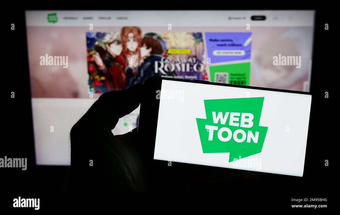 Person, die ein Mobiltelefon mit dem Logo des Digital Comic Company WEBTOON Entertainment Inc. Auf dem Bildschirm vor der Webseite hält. Konzentrieren Sie sich auf das Display des Telefons. Stockfoto