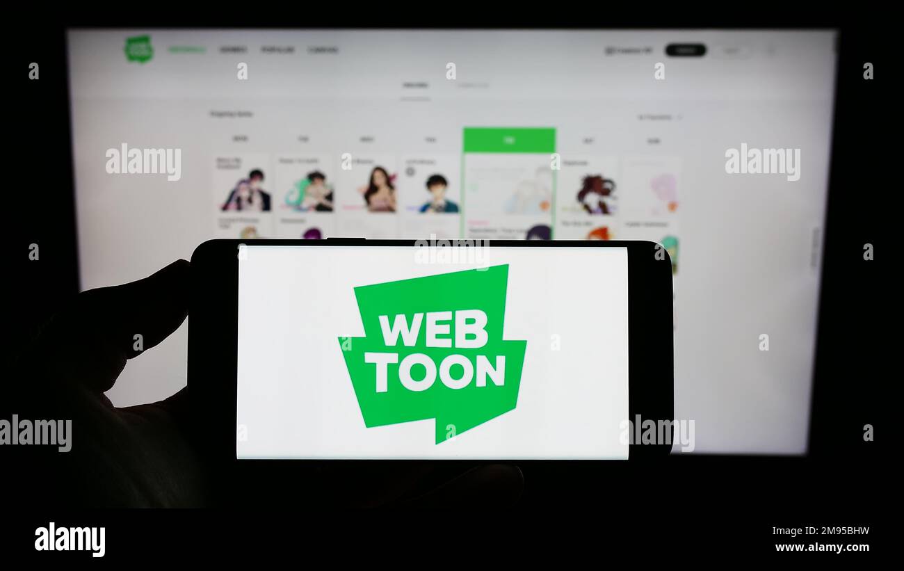 Person, die ein Mobiltelefon mit dem Logo der Digital Comic Company WEBTOON Entertainment Inc. Auf dem Bildschirm vor der Webseite hält. Konzentrieren Sie sich auf das Display des Telefons. Stockfoto