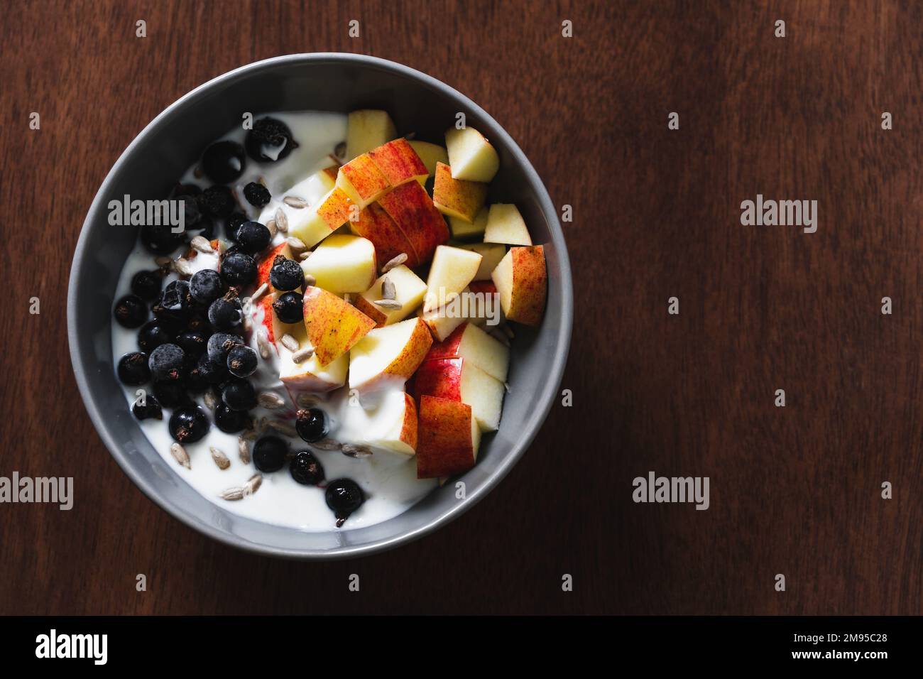 Gesunde Frühstückschüssel mit Obst und Joghurt auf einer hölzernen Oberfläche mit Scheiben von Apfel, schwarzen Johannisbeeren und Sonnenblumenkernen. Draufsicht, Kopierbereich. Stockfoto