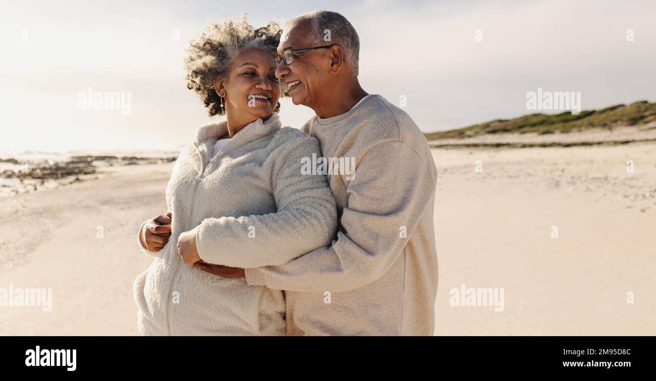 Reife Romantik am Strand. Glückliches Seniorenpaar lächelt und umarmt sich, während sie auf dem Strand standen. Liebevolles älteres Paar genießt es Stockfoto