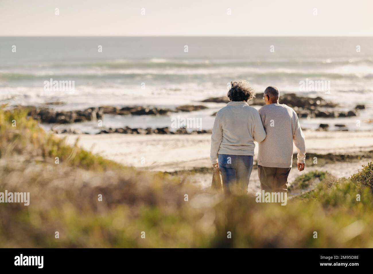 Rückblick auf ein romantisches Seniorenpaar, das zum Strand für ein Picknick ging. Sorgenfreies älteres Ehepaar, das nach seiner Pensionierung einen Badeurlaub macht. Stockfoto