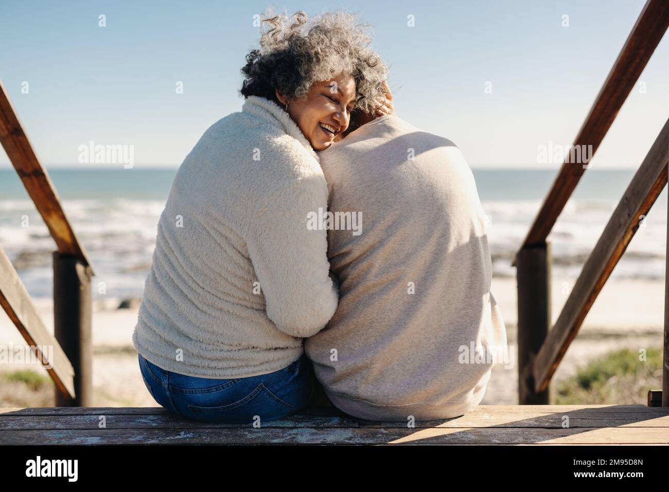 Rückblick auf eine glückliche ältere Frau, die fröhlich lächelt, während sie mit ihrem Mann vor dem Meer sitzt. Rentnerpaar, das Qualität verbringt Stockfoto