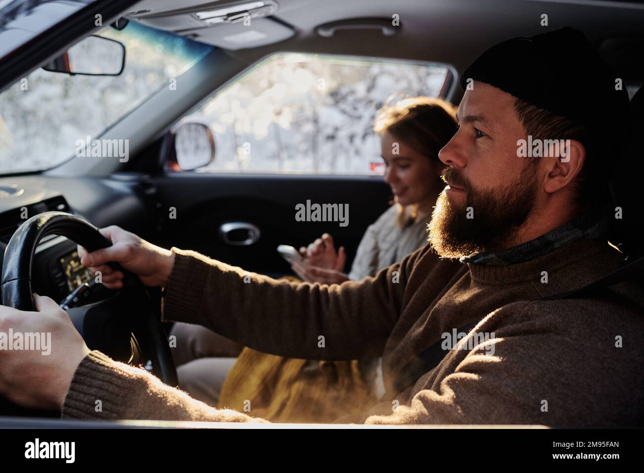 Ein bärtiger Mann, der sich auf das Fahren konzentriert, sitzt im Auto zusammen mit seiner Freundin Stockfoto