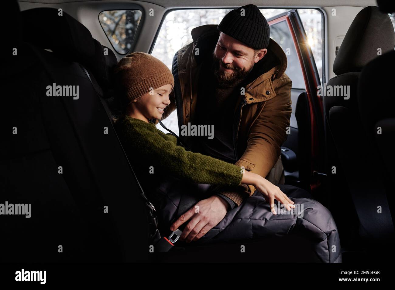 Glücklicher Vater, der seine Tochter auf den Rücksitz setzte und sie vor der Reise anschnallte Stockfoto