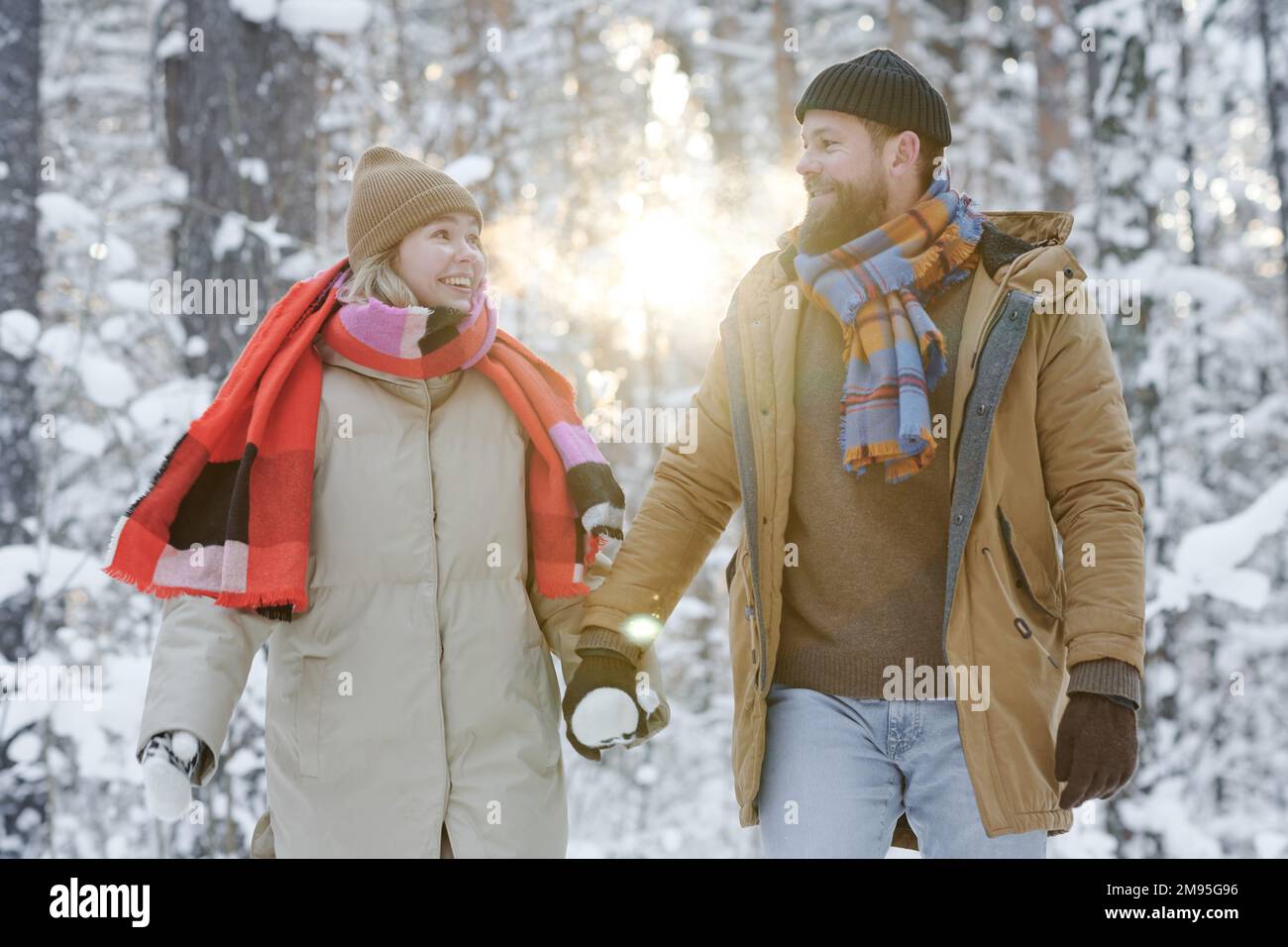 Ein junges glückliches Paar, das Händchen hält und im Winter zusammen im Wald spaziert Stockfoto
