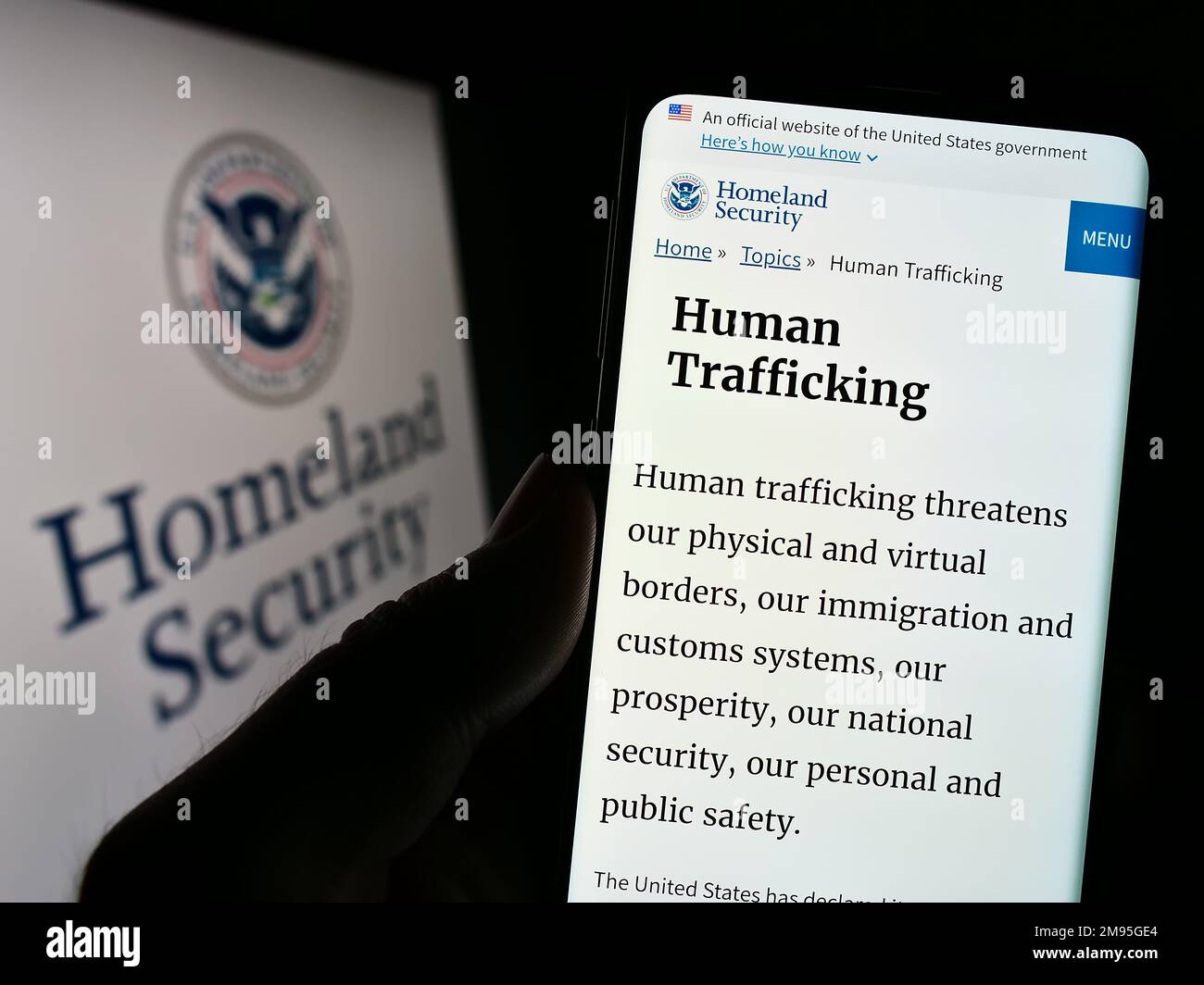 Person, die ein Mobiltelefon mit einer Webseite des US Department of Homeland Security (DHS) auf dem Bildschirm vor dem Siegel hält. Konzentrieren Sie sich auf die Mitte des Telefondisplays. Stockfoto