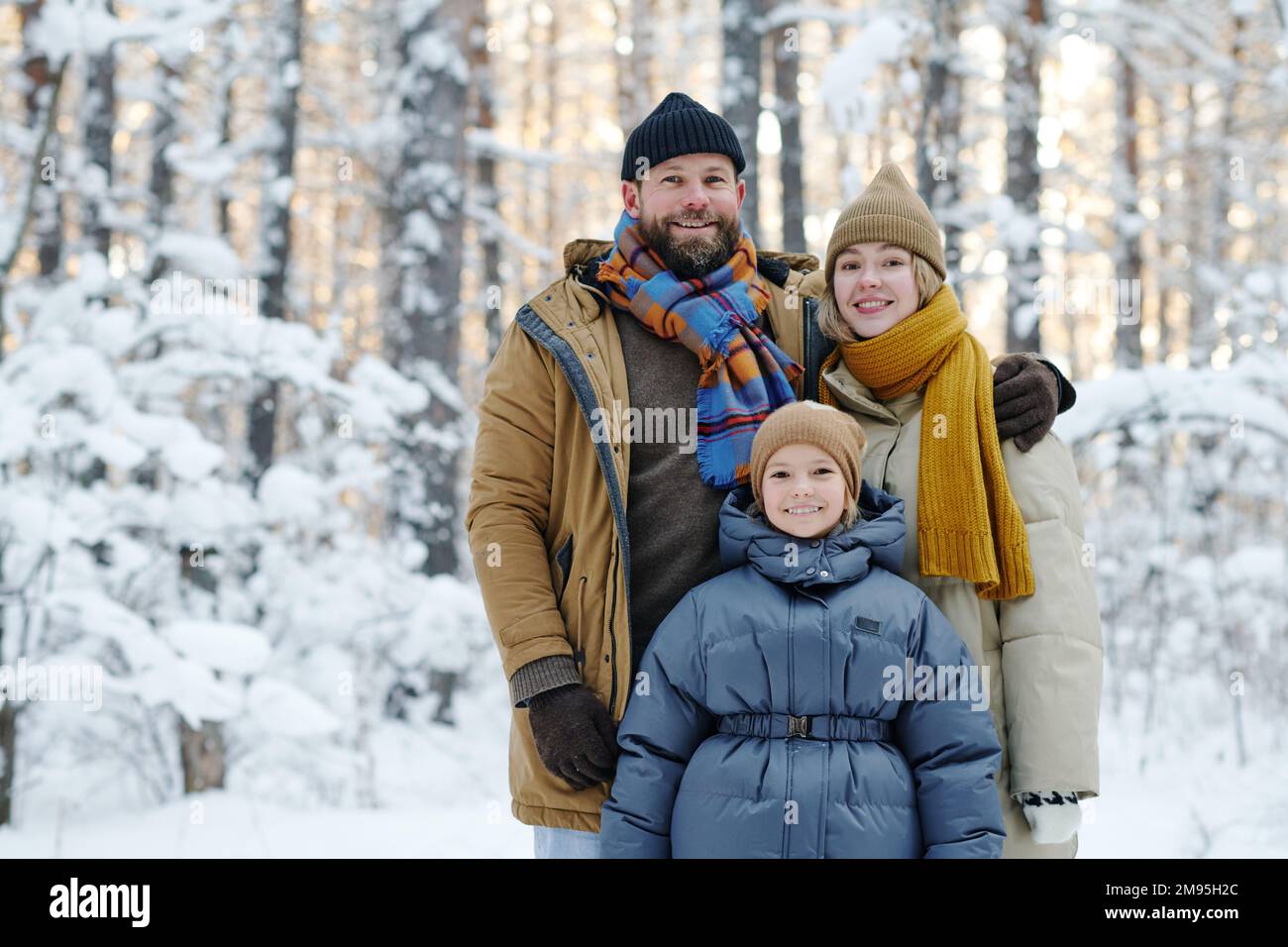 Porträt einer glücklichen Familie mit ihrer Tochter, die zusammen vor der Kamera lächelt und im Winterwald steht Stockfoto