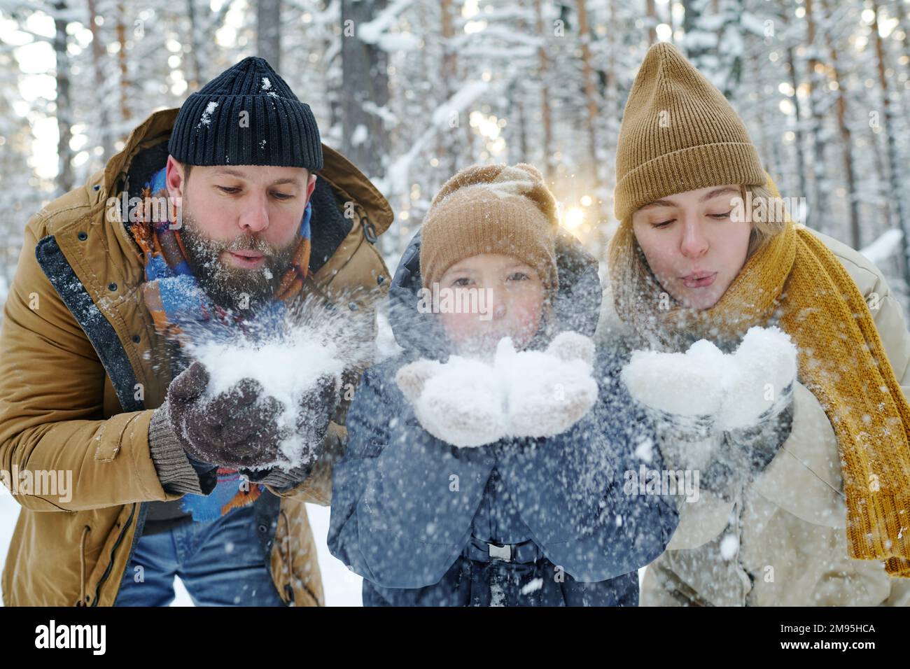 Porträt einer glücklichen dreiköpfigen Familie, die während des Spaziergangs im Park Schnee aus den Händen bläst Stockfoto
