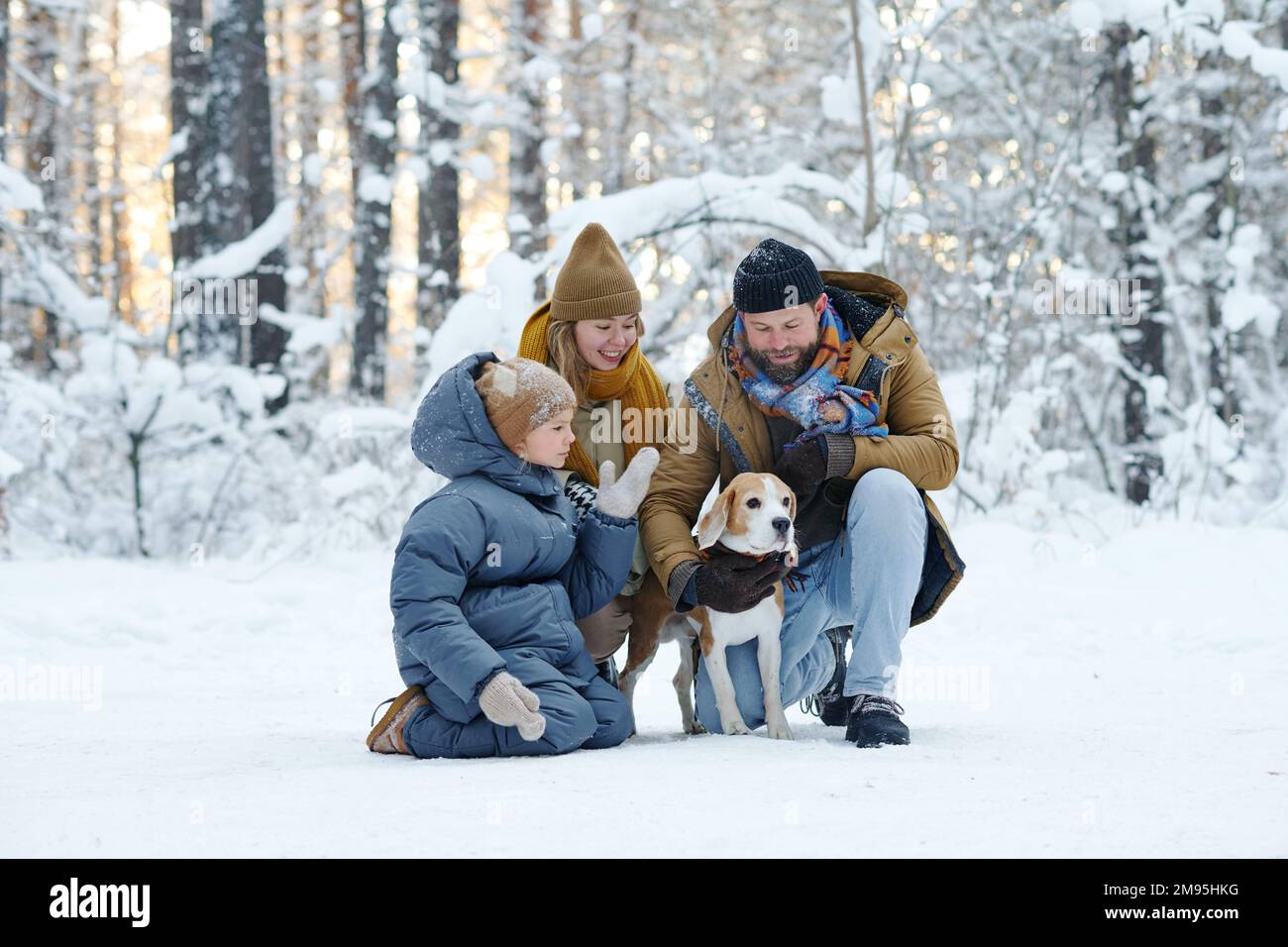 Eine dreiköpfige Familie, die während ihres Urlaubs mit einem Hund im Winterwald spazieren geht Stockfoto