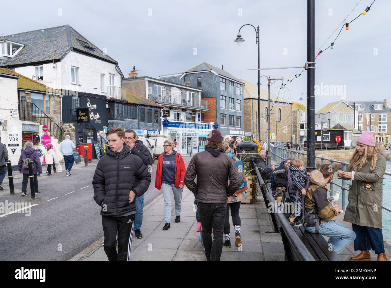 Leute, die an Geschäften und Restaurants auf der Wharf Road in einem kalten, kühlen St Ives in Cornwall in England vorbeispazieren. Stockfoto