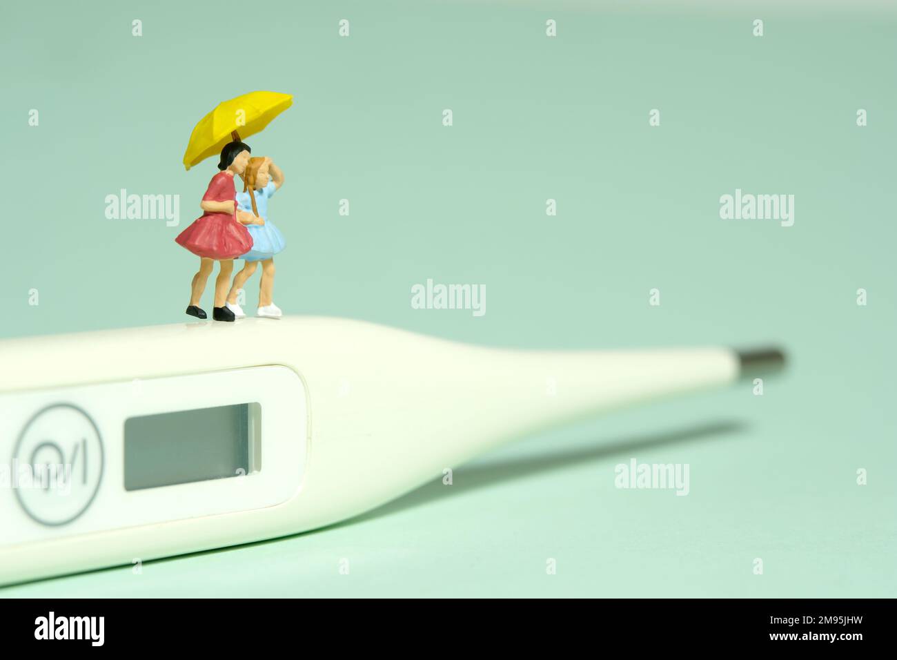 Miniatur-Menschen-Spielzeug-Figuren-Fotografie. Zwei Mädchen stehen über einem weißen Thermometer. Isoliert auf grünem Hintergrund. Bildfoto Stockfoto
