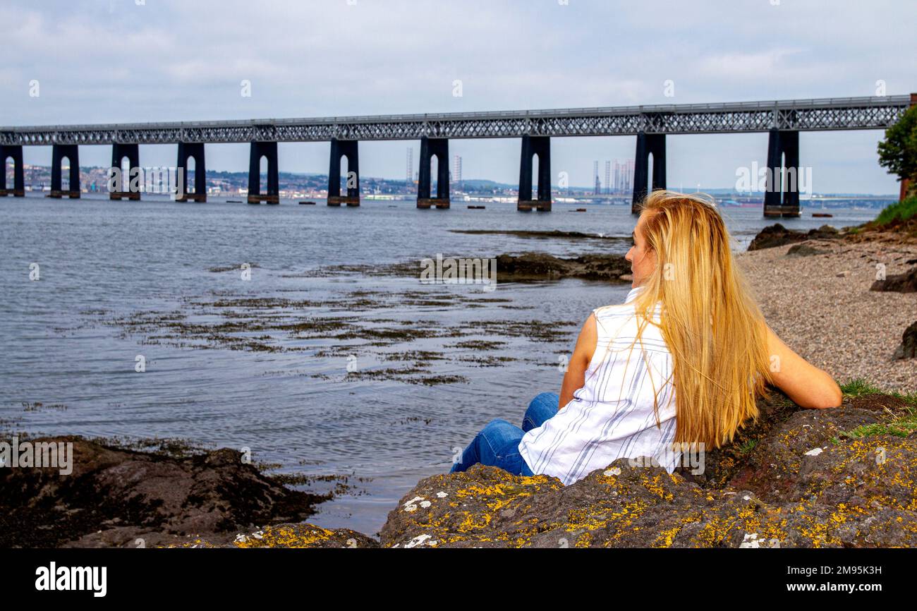 Rhianna Martin, eine wunderschöne blonde Frau, sitzt auf Felsen und bewundert die Aussicht am Wormit Beach in Fife County, Schottland, Großbritannien Stockfoto