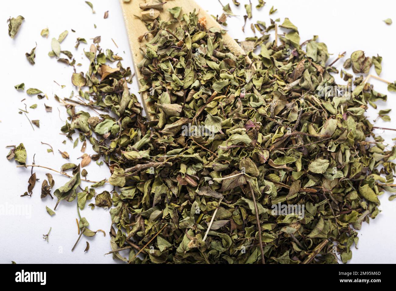 Rustikaler Holzlöffel und verstreute getrocknete Kräuter. Verschüttete kulinarische Zutaten. Weißer Hintergrund. Stockfoto