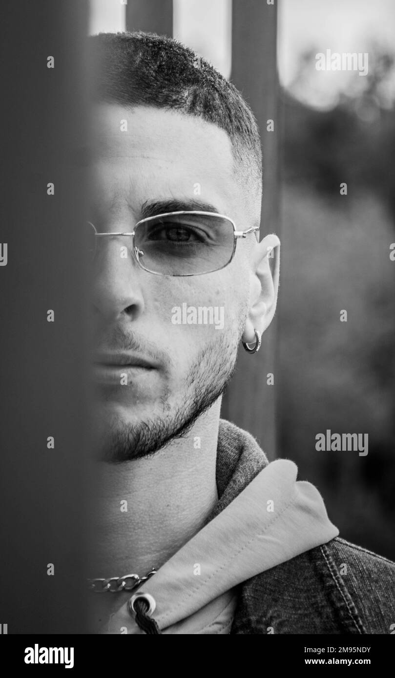 Eine vertikale Grauskalenaufnahme eines jungen Mannes mit Sonnenbrille, der in die Kamera schaut. Stockfoto