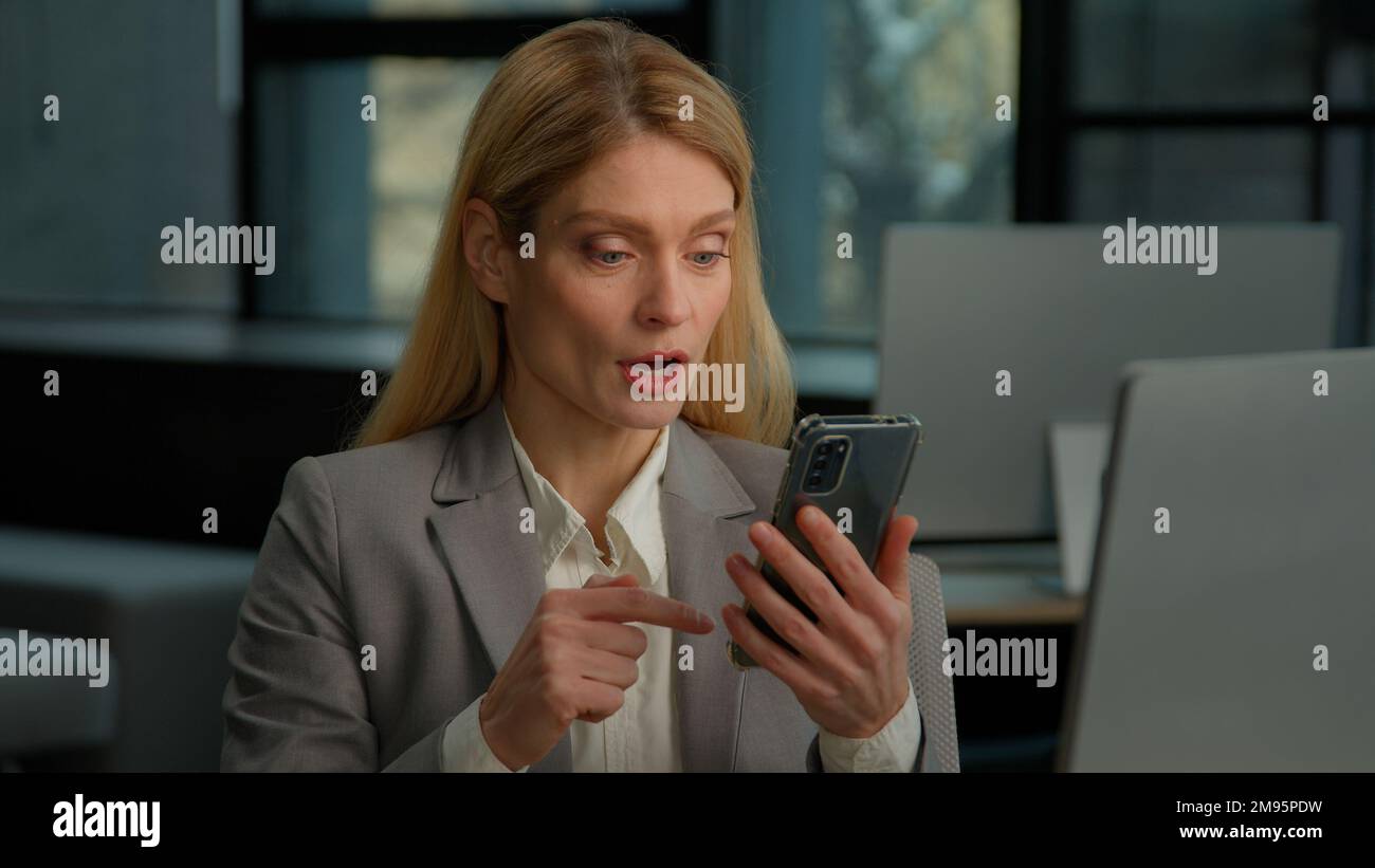 Kaukasische Erwachsene Mitarbeiterin mittleren Alters Büroangestellte Geschäftsfrau Unternehmerin drinnen, die beim Blättern auf dem Mobiltelefon schockiert war Stockfoto