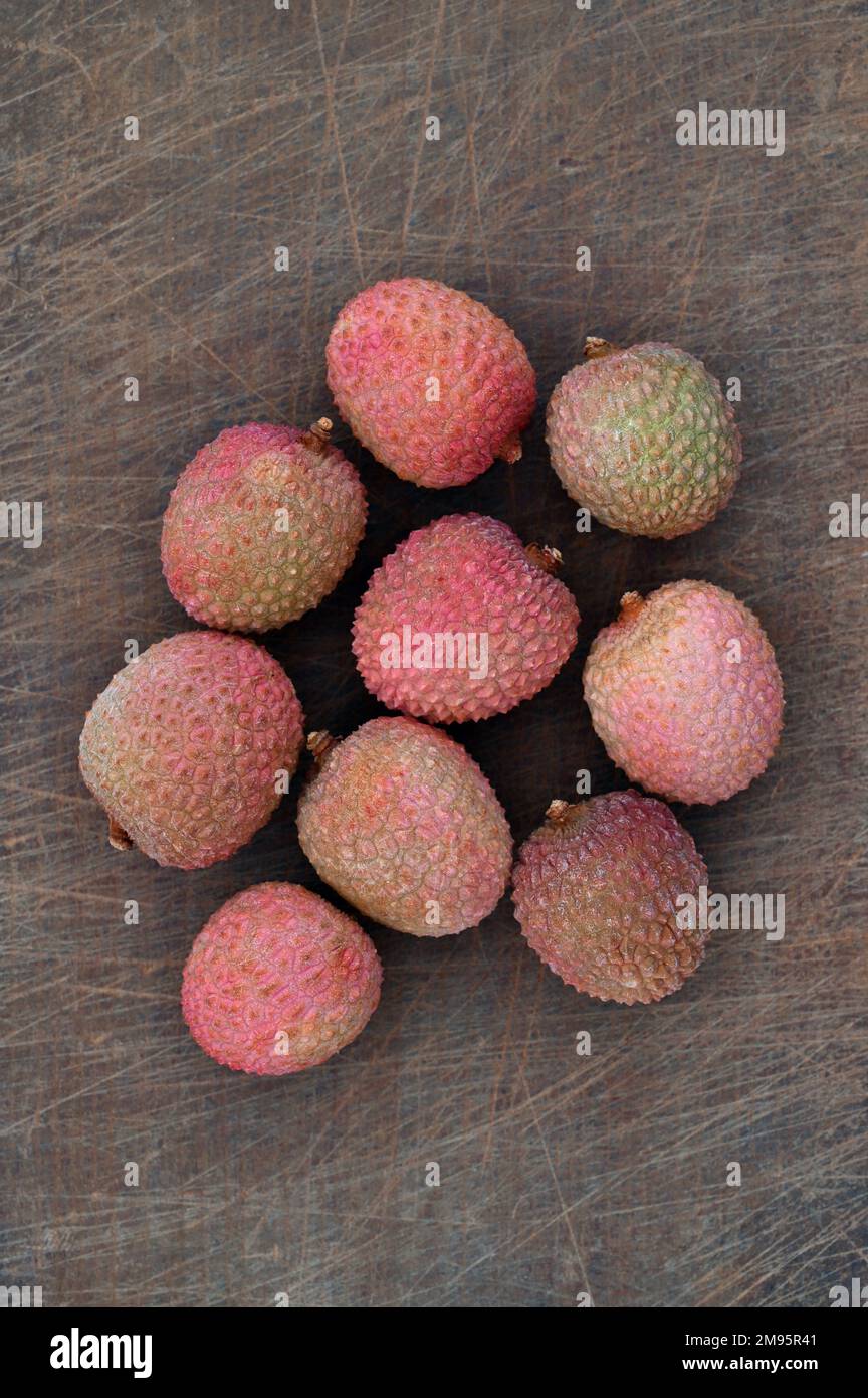 Neun reife pinkfarbene und grüne Lychee-Früchte liegen auf einem zerkratzten Schneidebrett Stockfoto
